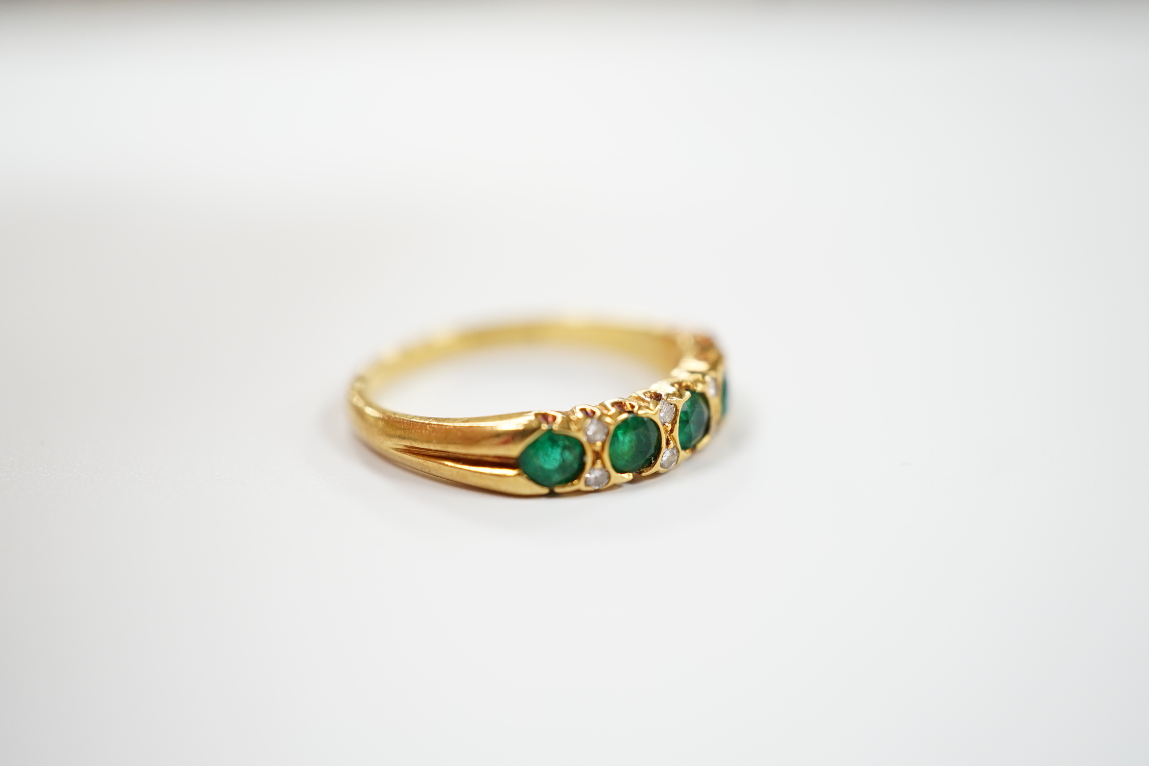 A modern 18ct gold and five stone emerald set half hoop ring, with diamond chip spacers, size K/L, gross weight 3 grams.